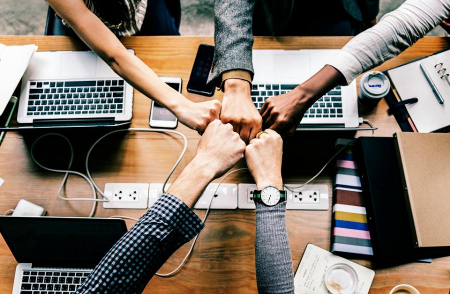 A team bumping fists over a desk of laptops
